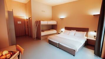 A hotel room with a large bed, a smaller bed on the left, a desk with a chair, and a fruit bowl on the desk.
