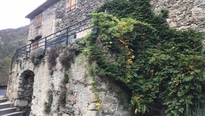 Ein Steinhaus mit rustikaler Fassade, einem hölzernen Balkon und einer Treppe, die zu einer oberen Ebene führt.