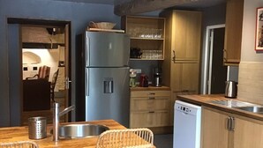 Eine kompakte Küche mit Kühlschrank, Geschirrspüler, Holzschränken und einem Essbereich mit Korbstühlen.
