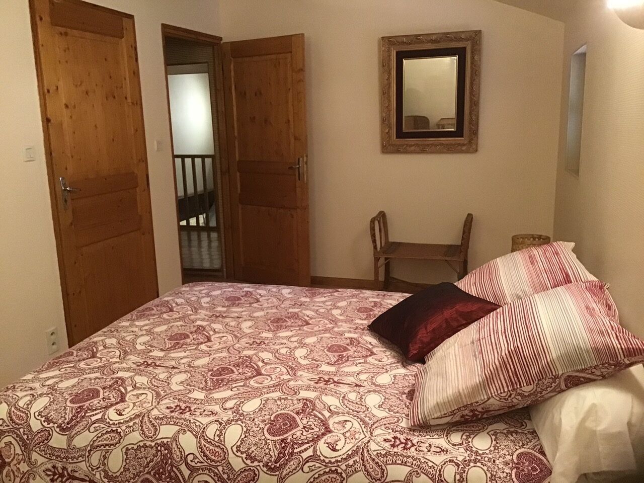 Een slaapkamer met een bed, twee houten deuren, een stoel en een spiegel aan de muur.