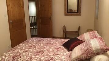 Een slaapkamer met een bed, twee houten deuren, een stoel en een spiegel aan de muur.
