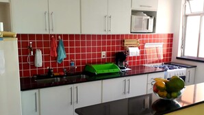 A kitchen with white cabinets, a red tiled backsplash, a green cutting board, a coffee maker, and a fruit bowl on the counter. - Casa Babilônia (Rio de Janeiro)