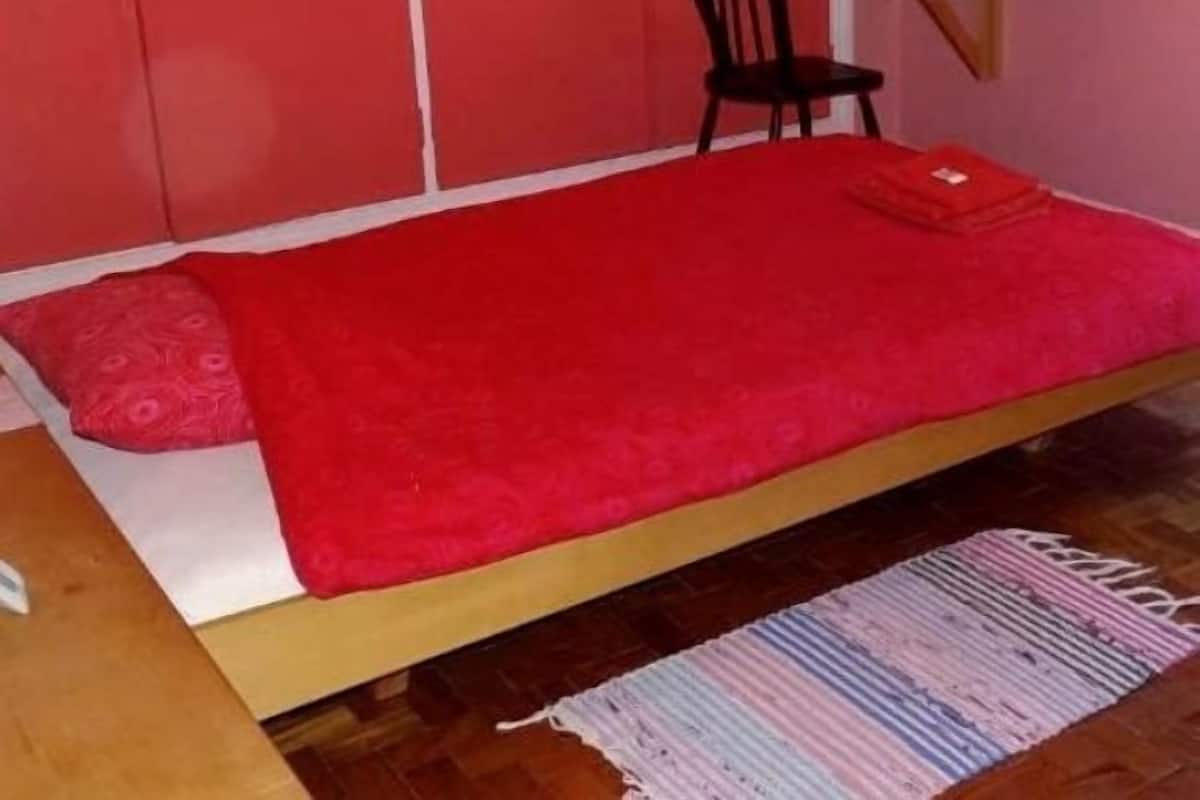A small room with a single bed, a chair, a small table, and a rug.
