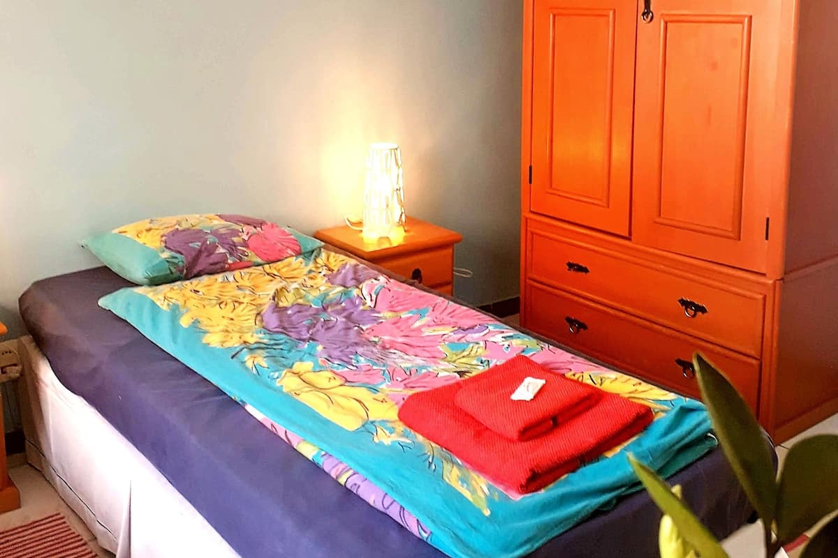 A bedroom with a bed, a nightstand, a dresser, and a lamp.