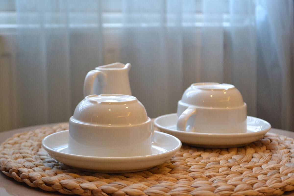 Two white ceramic teapots and cups on woven placemats.