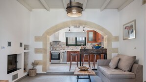 Een moderne keuken met een boog die leidt naar een zithoek, met een bank, een houten tafel en een televisie.
