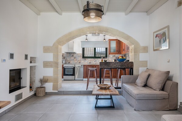 A modern kitchen with an archway leading to a dining area, featuring a sofa, a wooden table, and a TV.