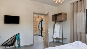 Een moderne hotelkamer met een bed, een televisie, een zithoek en uitzicht op een stenen bogenpoort.