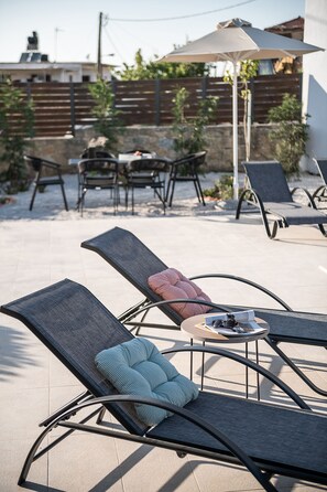 A patio area with lounge chairs, a table with a magazine and sunglasses, and a large umbrella.