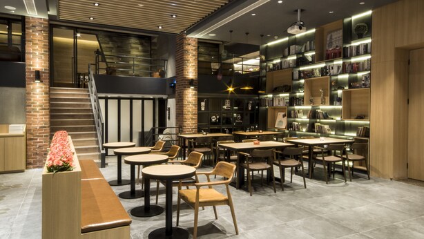 Moderni ravintola, jossa on tiiliseinä, puupöydät ja kirjahylly.