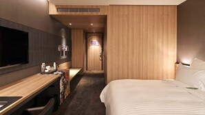Moderni hotellihuone, jossa on suuri sänky, taulutelevisio, työpöytä ja suihkutila.