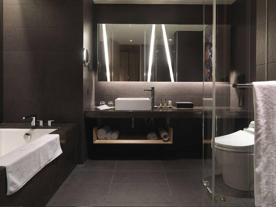 A modern bathroom with a large mirror, a bathtub, a sink, and a toilet.