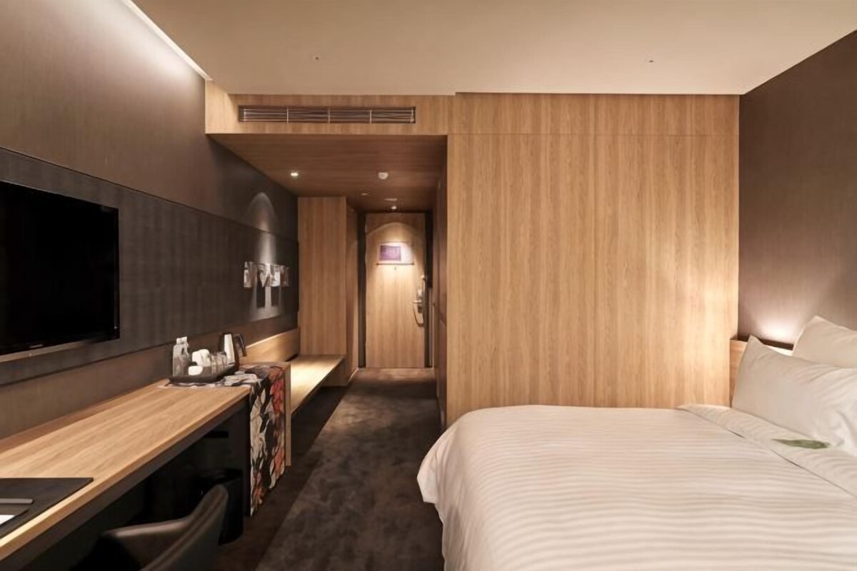 A hotel room with a bed, a desk, a TV, and a bathroom door.