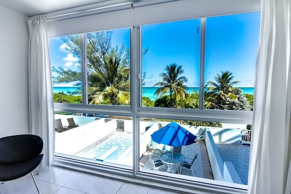A room with a large window overlooking a pool and a beach.