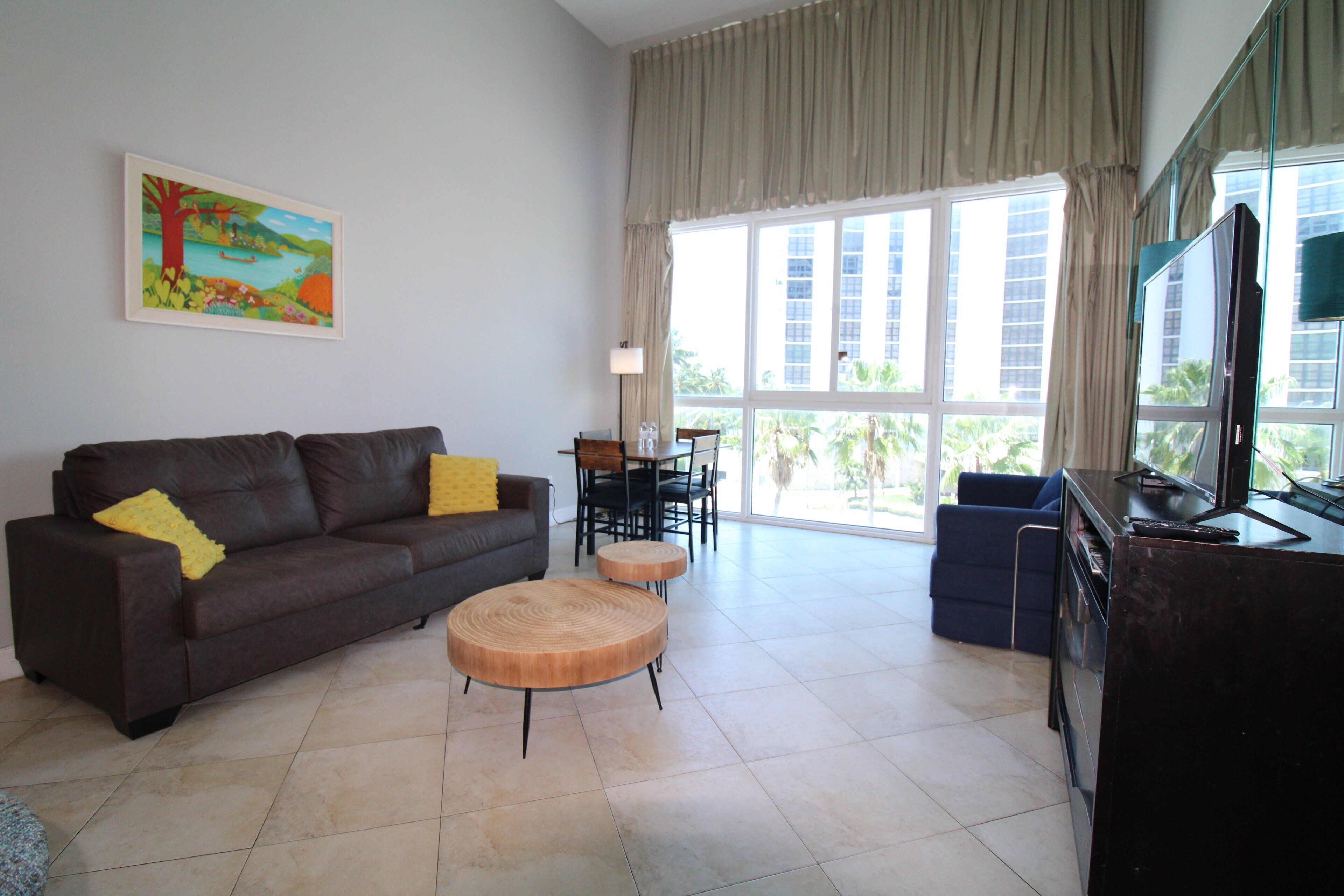 A living room with a sofa, a coffee table, a TV, and a dining area with chairs and a table.