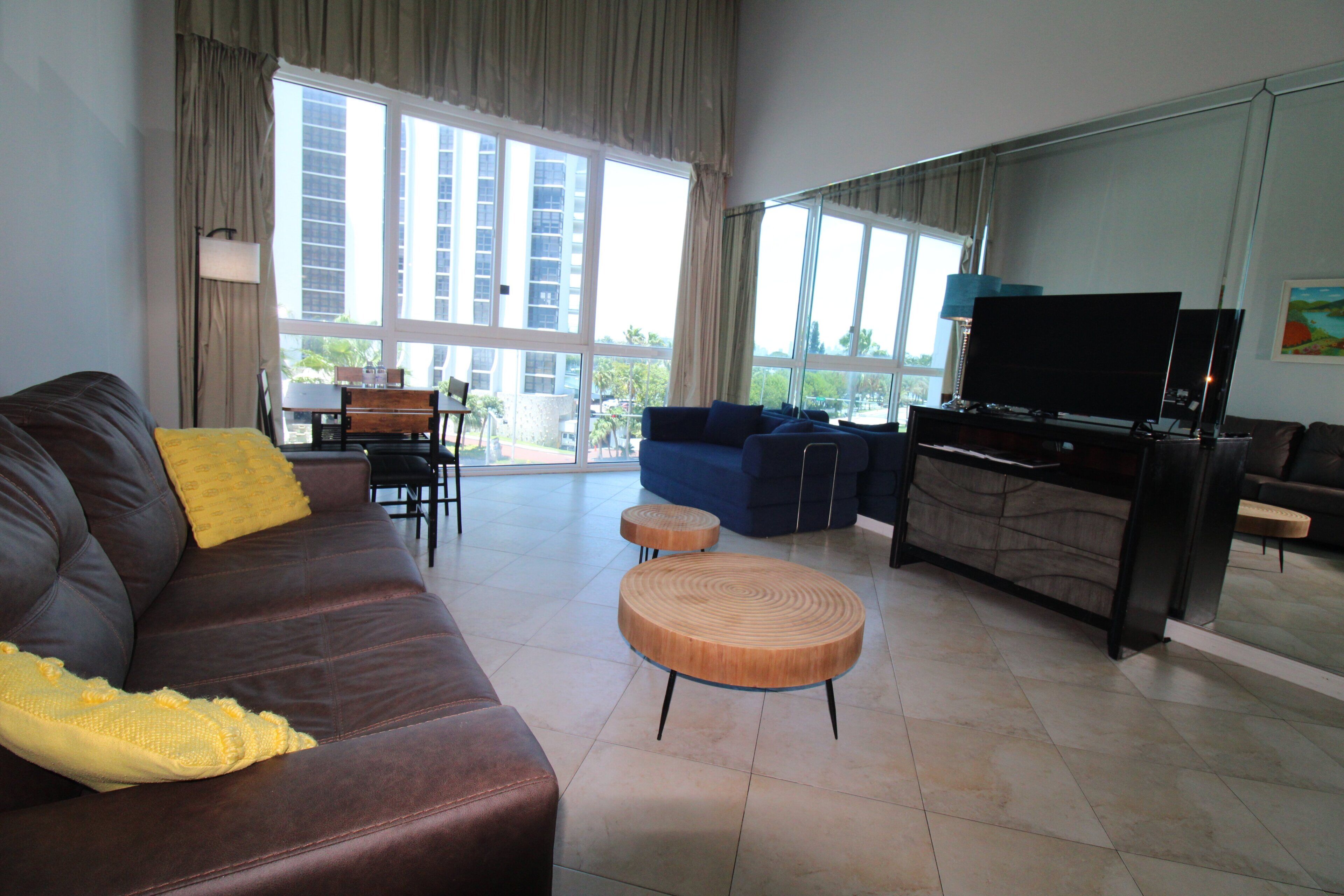 A modern living room with a brown leather sofa, a blue sofa, a wooden coffee table, and a flat-screen TV.