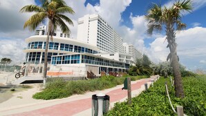 A modern hotel with a curved facade, palm trees, and a pathway leading to the entrance. - Castle B17 Pool, Tennis, Beach Access, Gym and Free Parking! (Miami Beach)