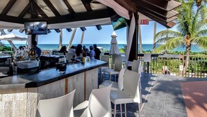 An outdoor bar area with a view of the ocean, white chairs, and a bar counter.