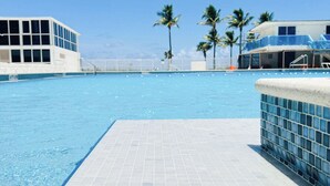 A swimming pool with tiled flooring, palm trees, and buildings in the background. - Castle 1033  Ocean view studio, Pool and Beach Access, FREE Parking, Tennis and more! (Miami Beach)