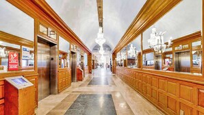 Un vestíbulo de hotel con paneles de madera, suelo de mármol y candelabros.