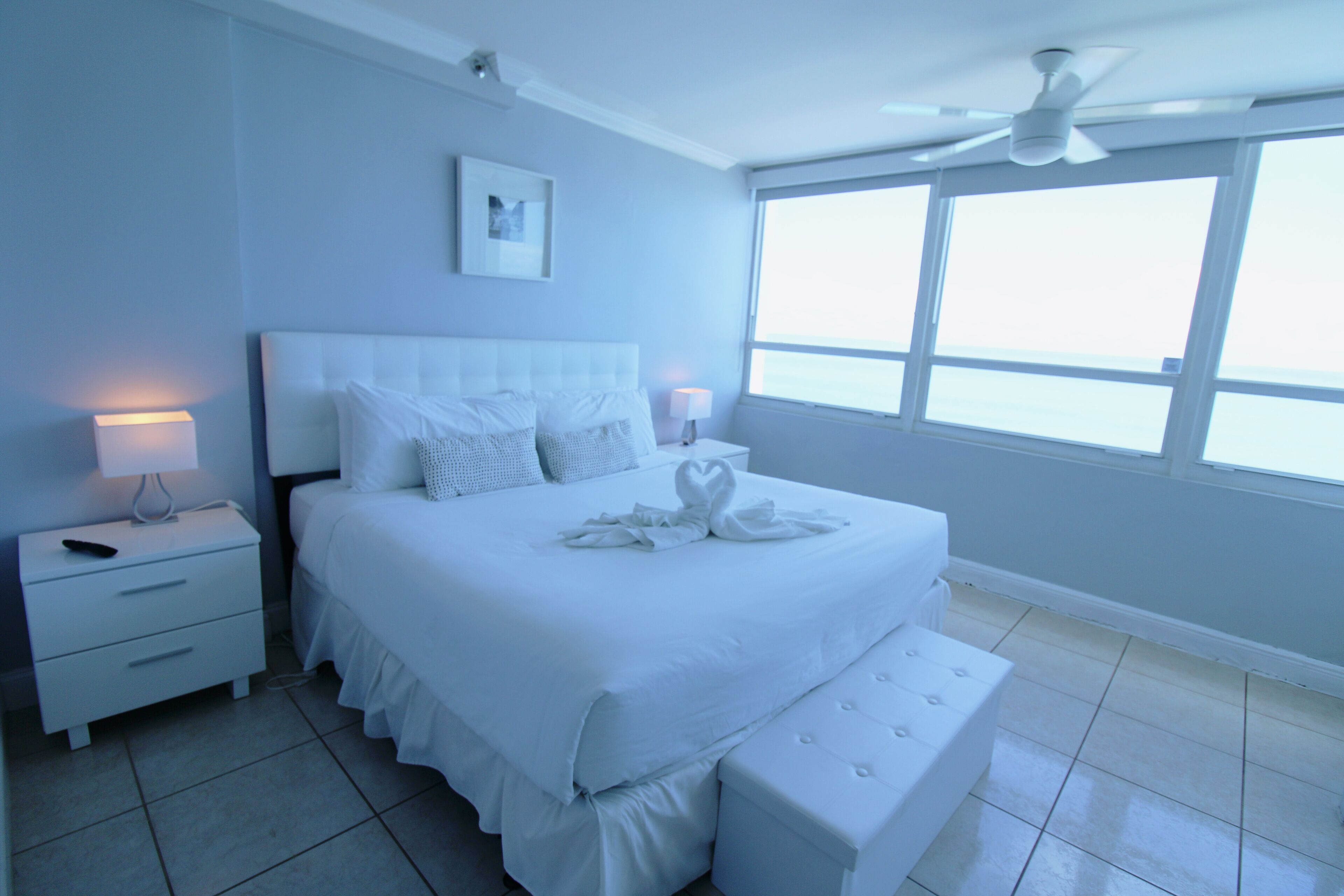 A bedroom with a large bed, bedside tables, a ceiling fan, and a window.