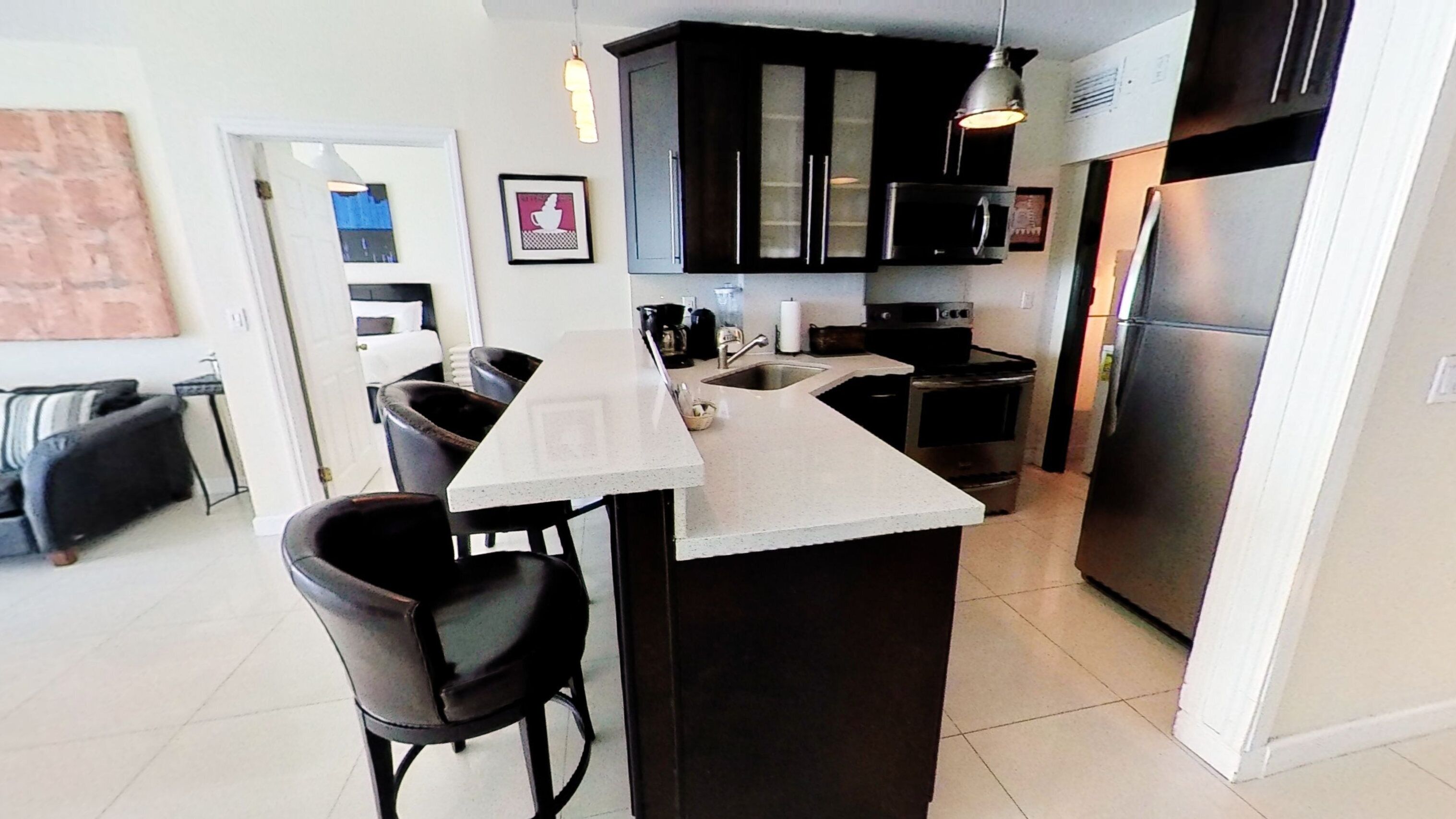 A modern kitchen with dark cabinetry, a central island with bar stools, a built-in oven, and a stainless steel refrigerator.
