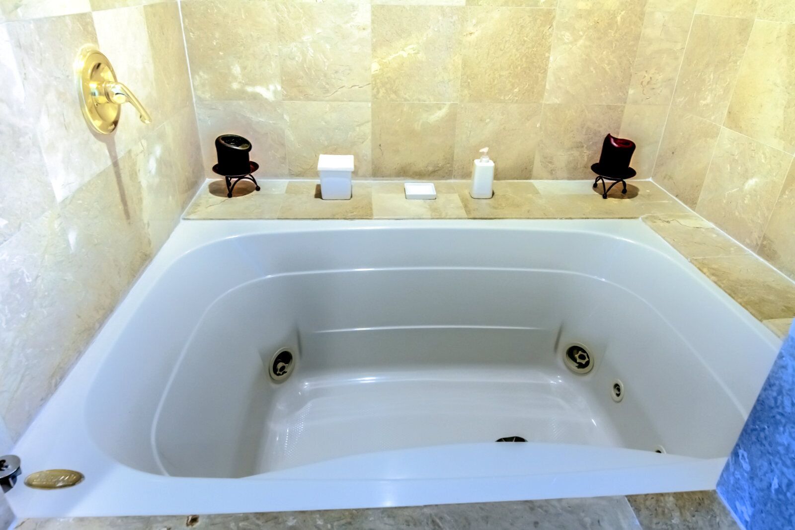 A large white bathtub with two black chairs and a small table with a bottle and a box on top.