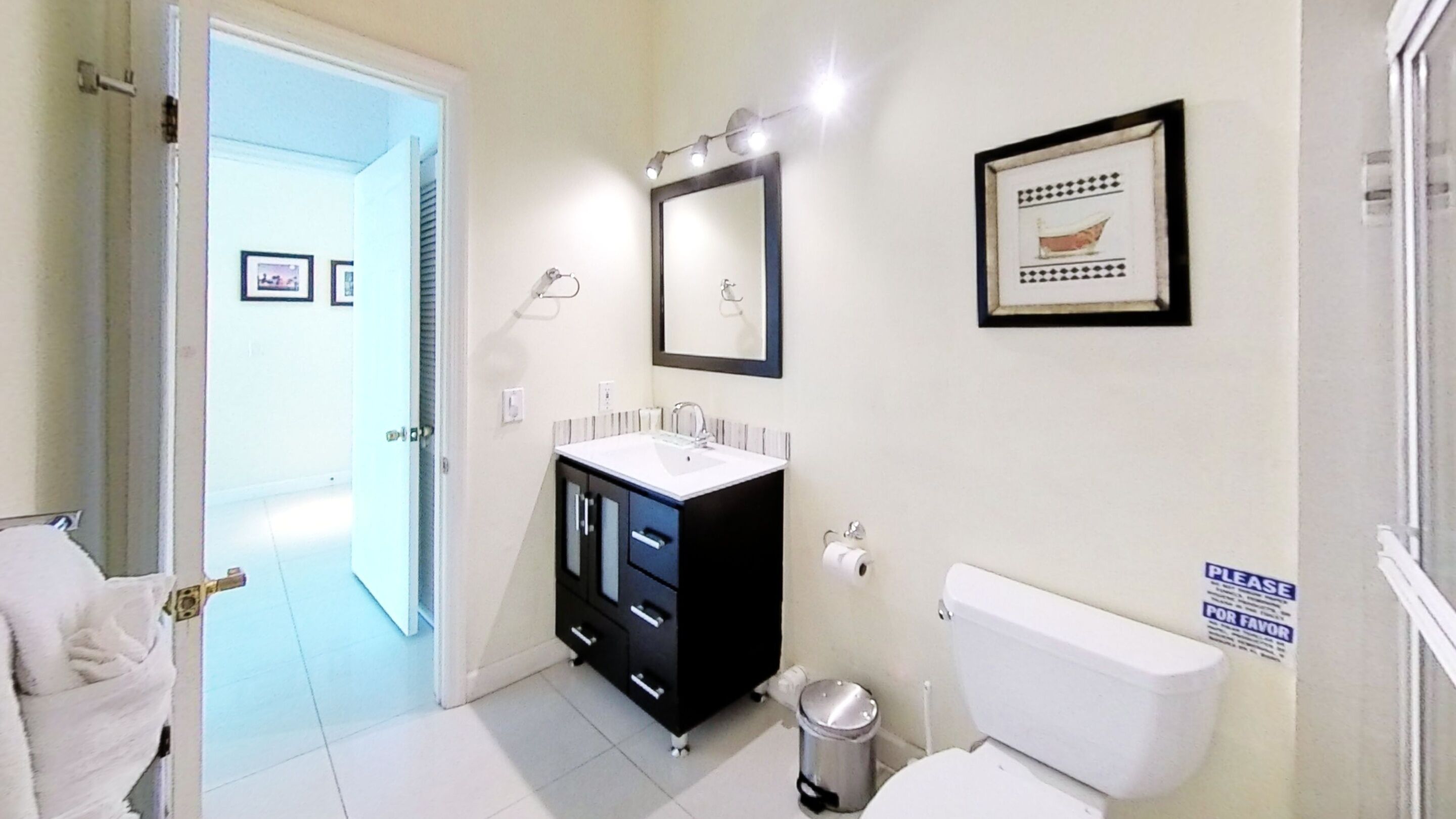 A bathroom with a white toilet, a black cabinet with a sink, a mirror, and a framed picture on the wall.