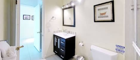 A bathroom with a white toilet, a black cabinet with a sink, a mirror, and a framed picture on the wall.