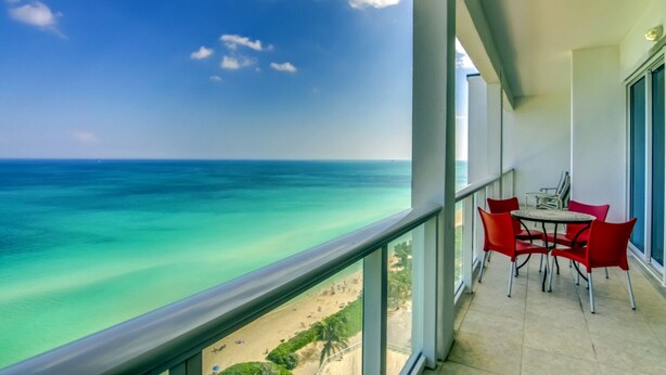 A balcony with a view of the ocean, a table with chairs, and a window overlooking the beach. - Castle PH3 Oceanfront Penthouse with Free parking, Gym and direct beach access! (Miami Beach)