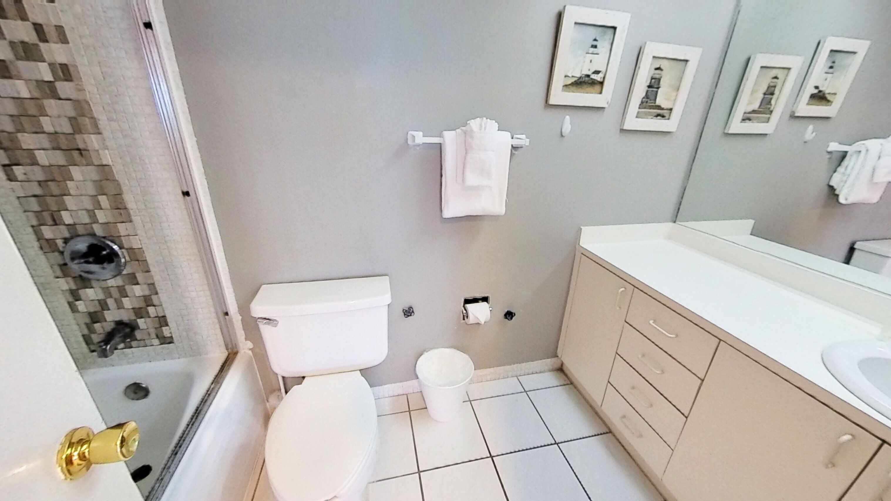 Une salle de bain avec des toilettes, un lavabo et une douche. Des serviettes sont accrochées au mur, et il y a une petite poubelle.