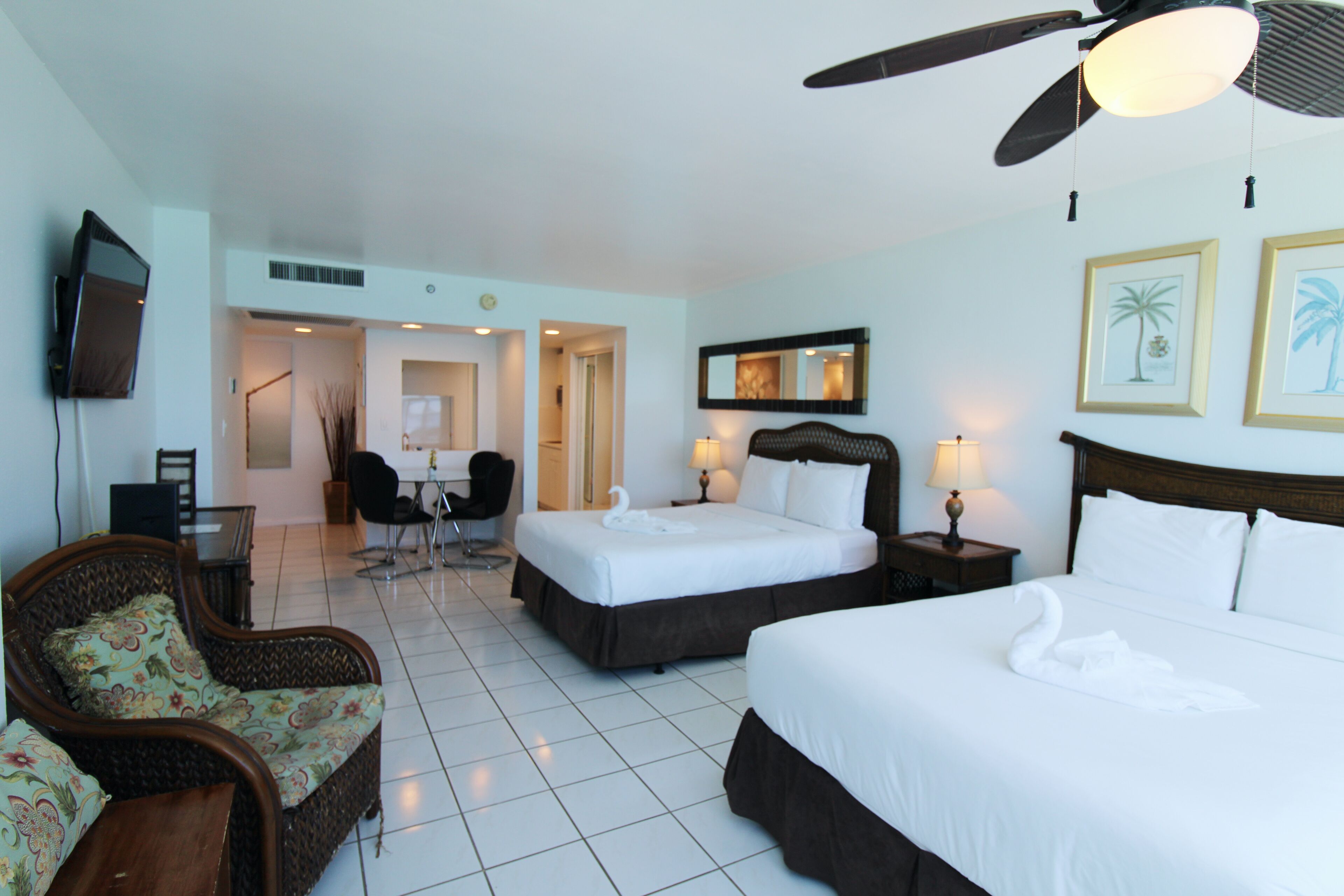 A hotel room with two beds, a dining area, a TV, and a ceiling fan.