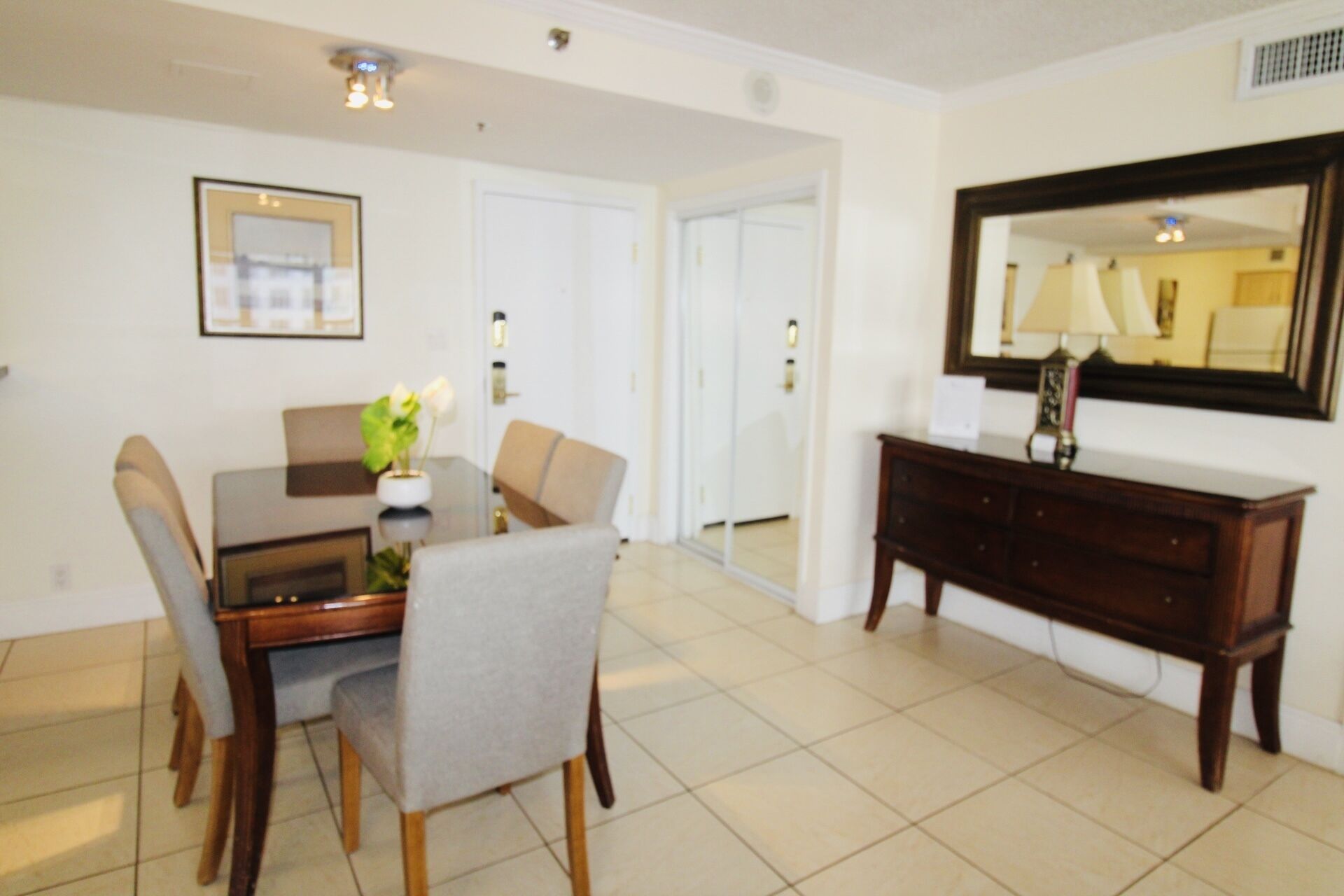 A dining area with a table, chairs, a vase with flowers, a mirror, and a cabinet.