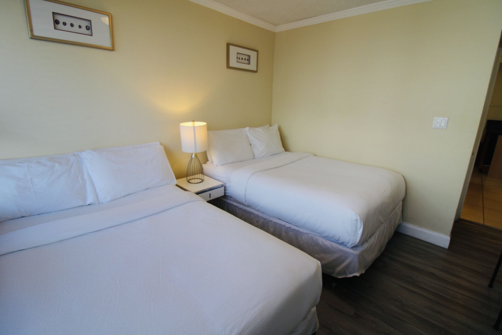 Habitación de hotel con dos camas individuales, una mesita de noche con lámpara y un enchufe en la pared.