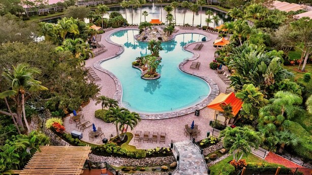 A large, curved swimming pool surrounded by palm trees and lounge chairs, with a view of the surrounding landscape. - Resort-style condo - close to beaches and downtown Naples. (Naples)