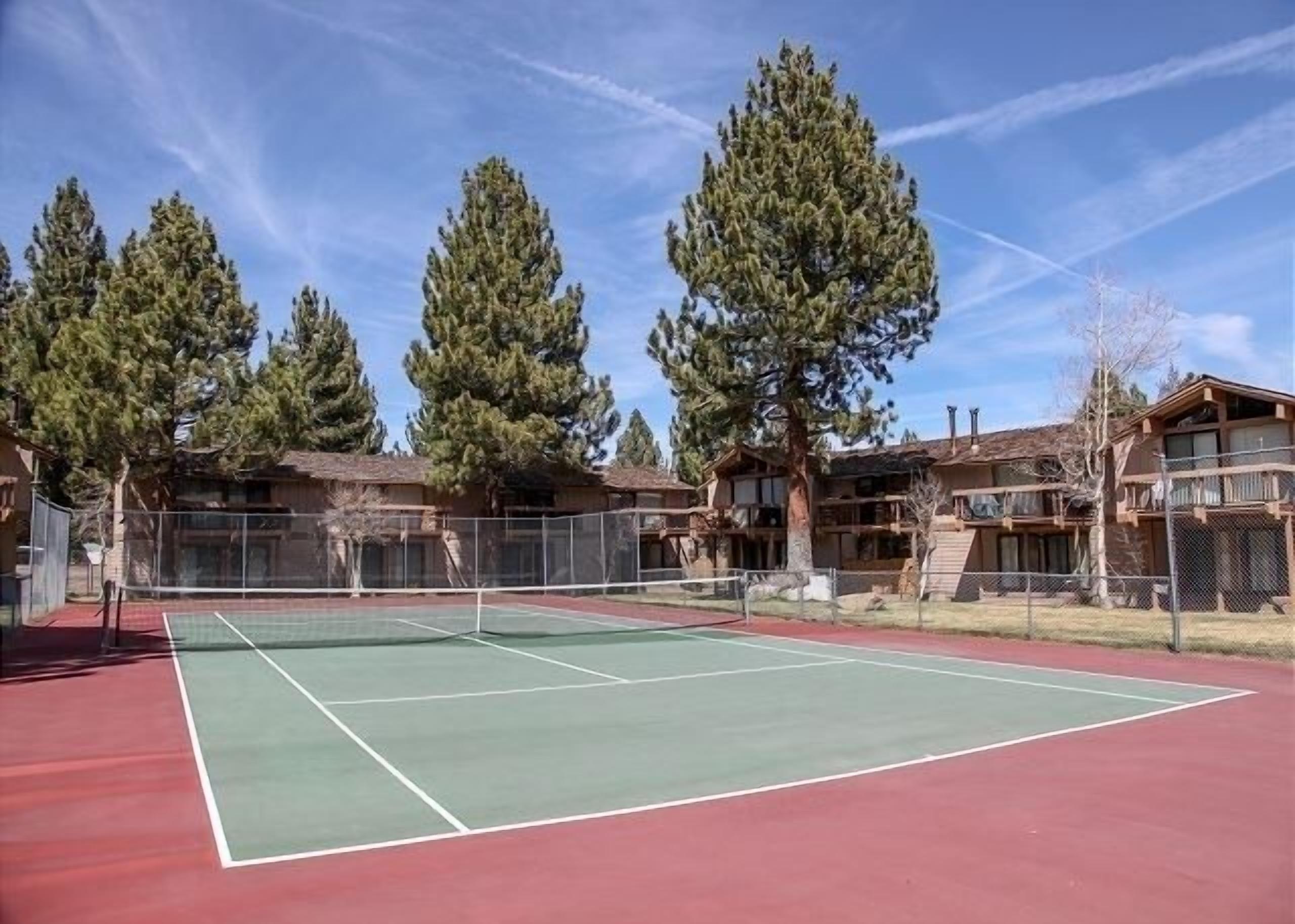 Una cancha de tenis al aire libre rodeada de árboles y edificios.
