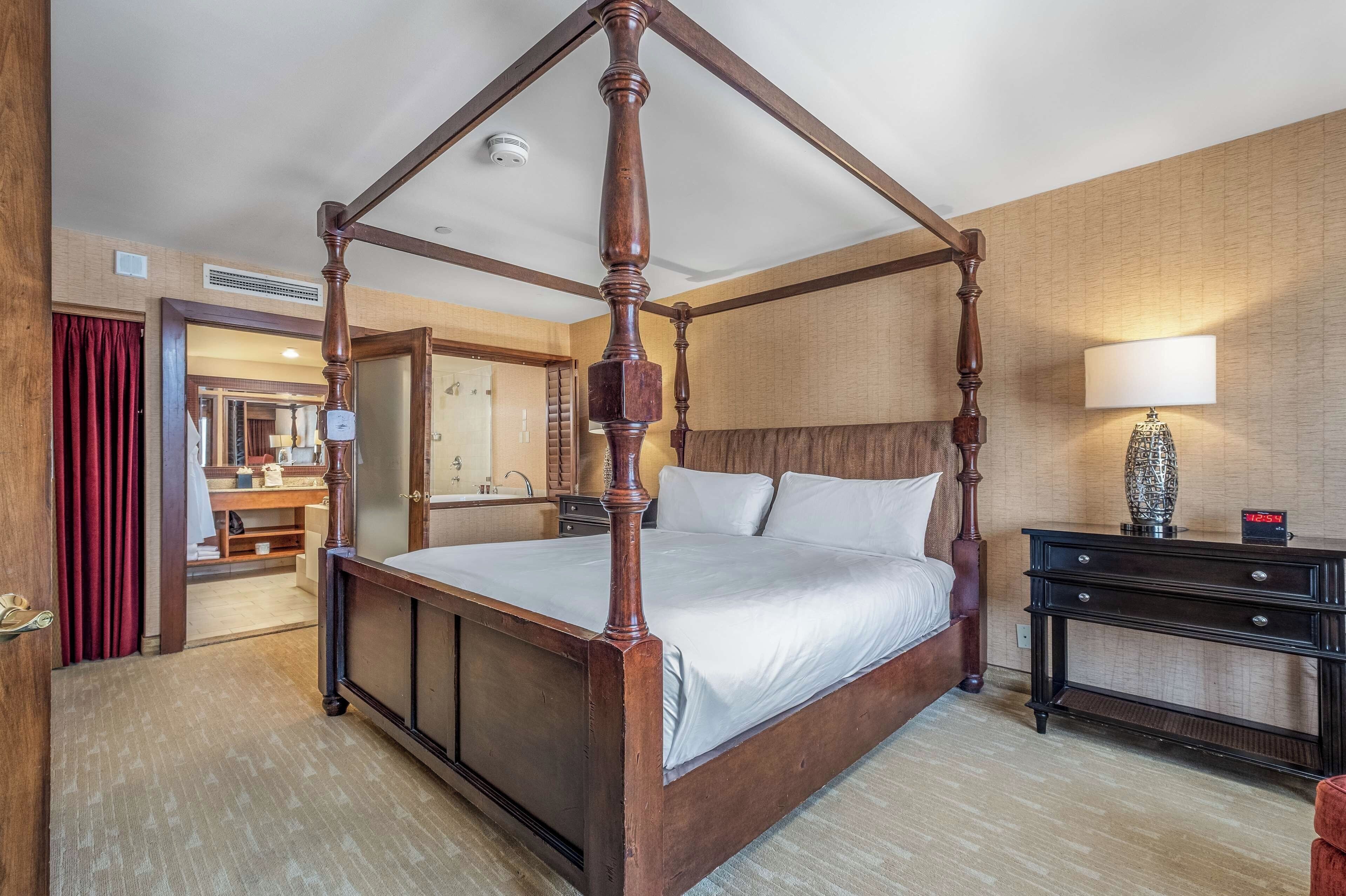 Cama de dossel em quarto de hotel com piso de madeira, mesa de cabeceira e espelho.