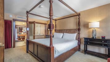 Cama de dossel em quarto de hotel com piso de madeira, mesa de cabeceira e espelho.