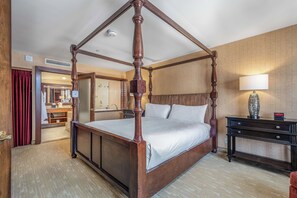 Una cama con dosel en una habitación de hotel con suelo de madera, una mesita de noche y un espejo.