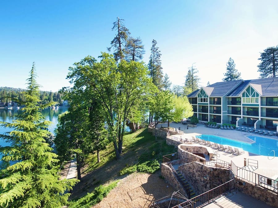 Um hotel com piscina, escadaria de pedra e vista para um lago rodeado de árvores.