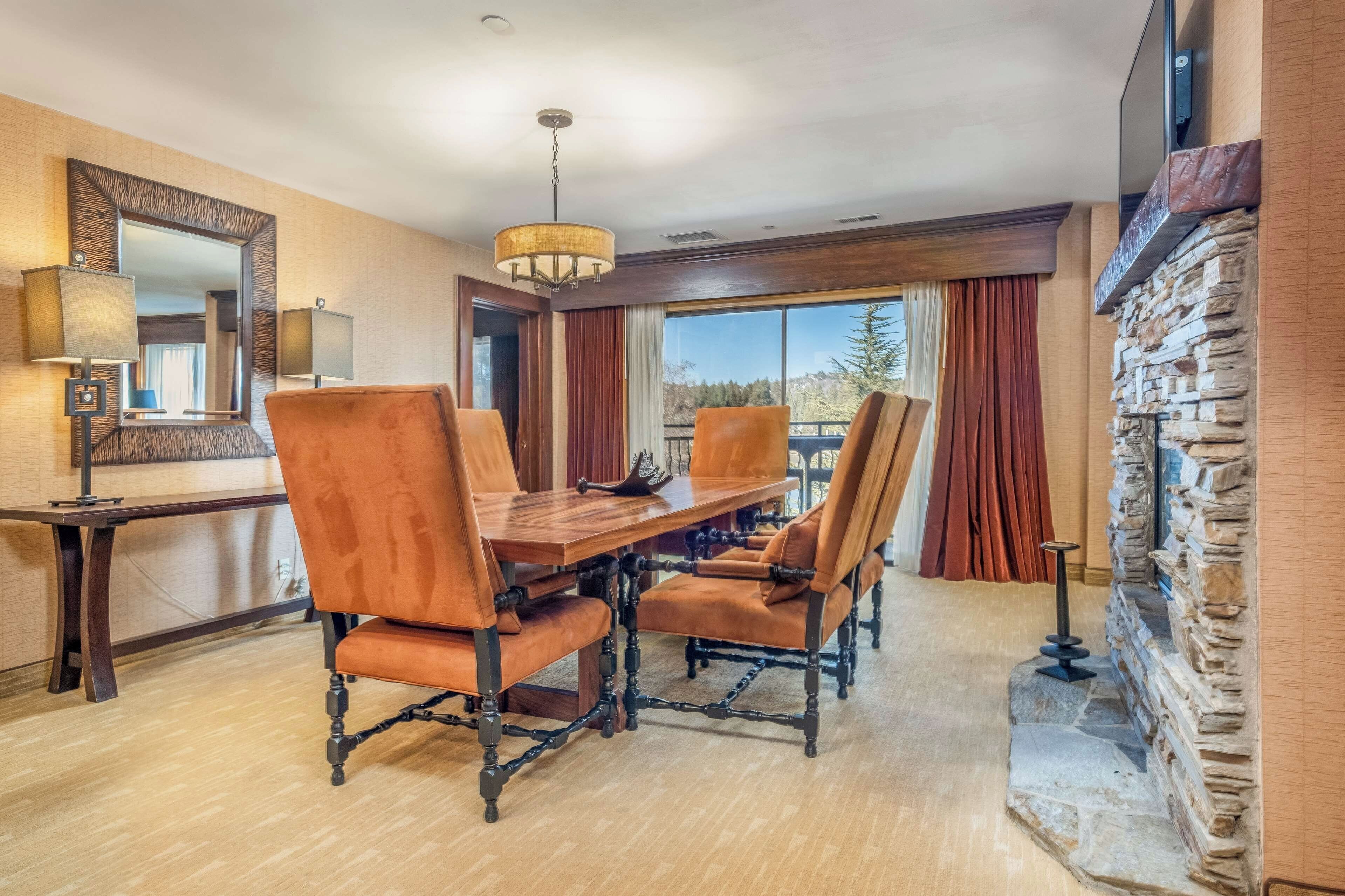 A dining area with a wooden table and chairs, a chandelier, and a stone wall.