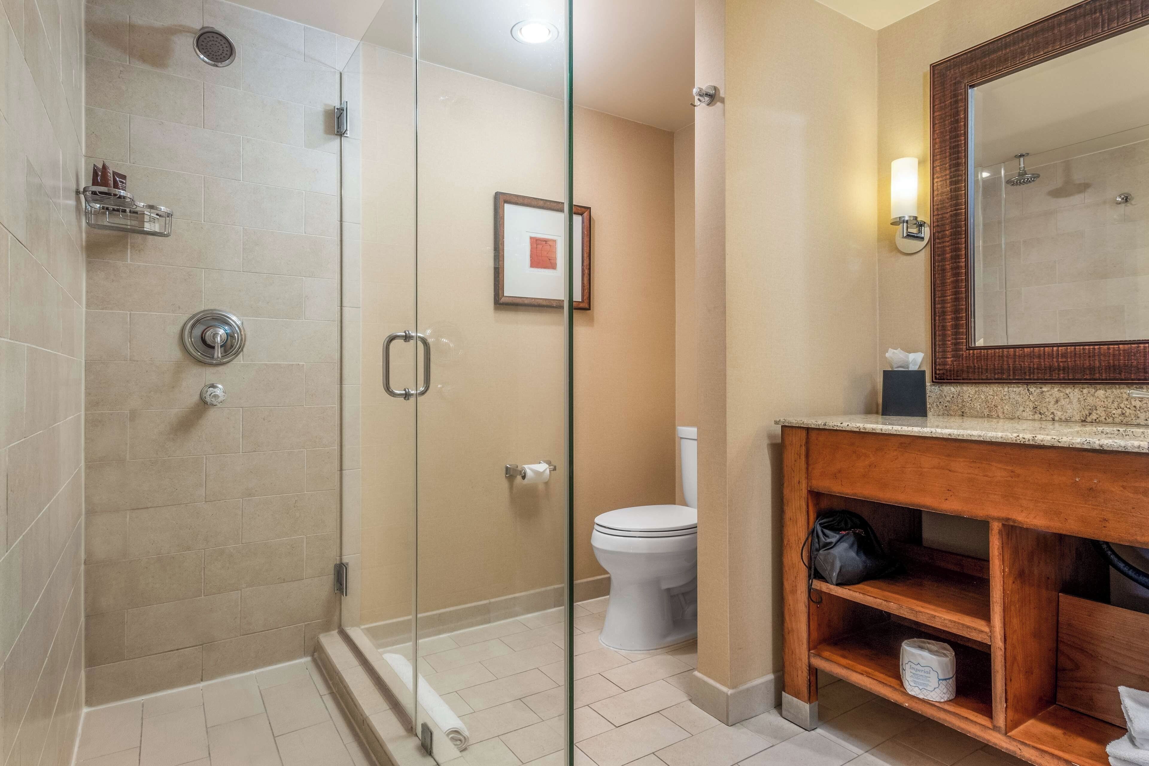 Un baño moderno con ducha de vidrio, inodoro y tocador de madera con espejo.
