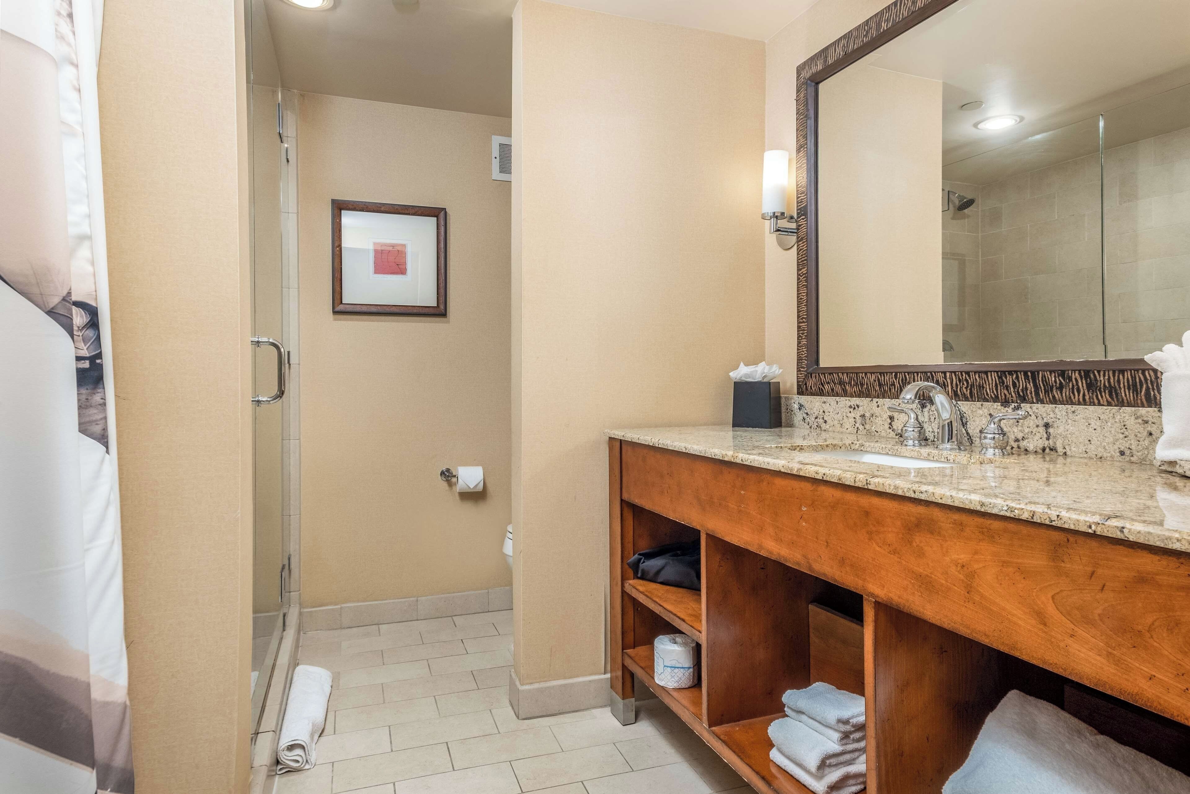 A hotel bathroom with a shower, a sink with a mirror, and a towel rack.