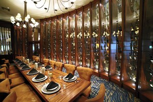 Comedor formal con una larga mesa dispuesta para una comida, rodeado de altos armarios de madera que exhiben botellas de vino.