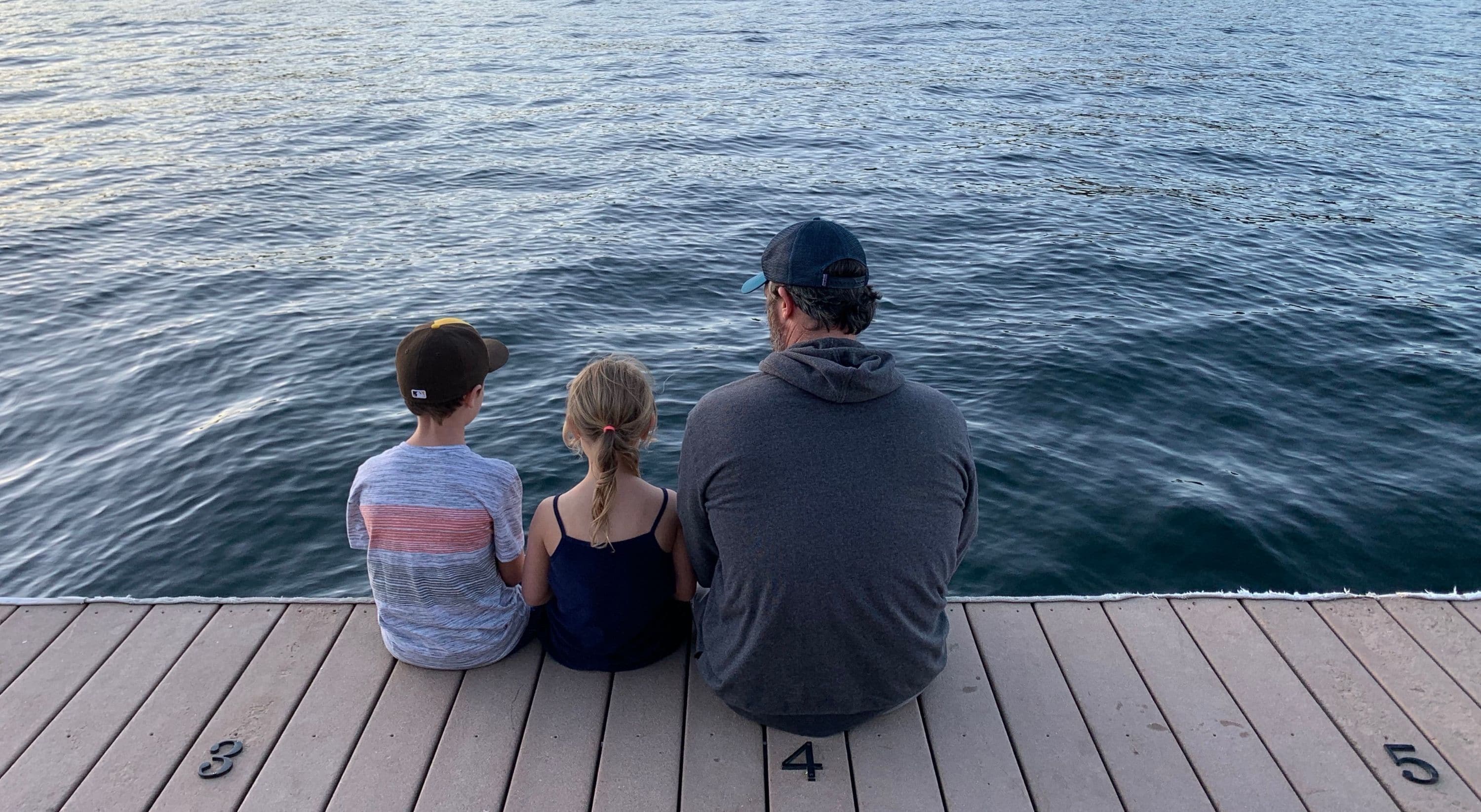 Three people sitting on a wooden deck overlooking a body of water.