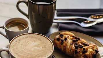 Una mesa con una taza de metal, una taza de café y un pastel en un plato.