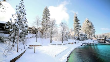 Un paisaje nevado con cielo azul despejado, una masa de agua y varios edificios con nieve en los tejados.