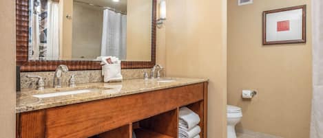 A bathroom with a wooden vanity, two sinks, a mirror, a toilet, and a shower curtain.