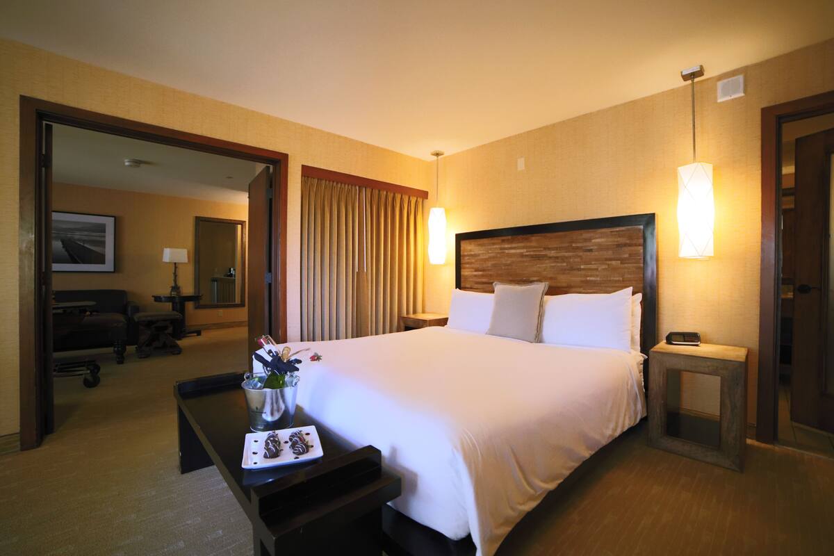 Habitación de hotel con una cama grande, mesitas de noche, un escritorio con silla, un espejo y vistas al pasillo.