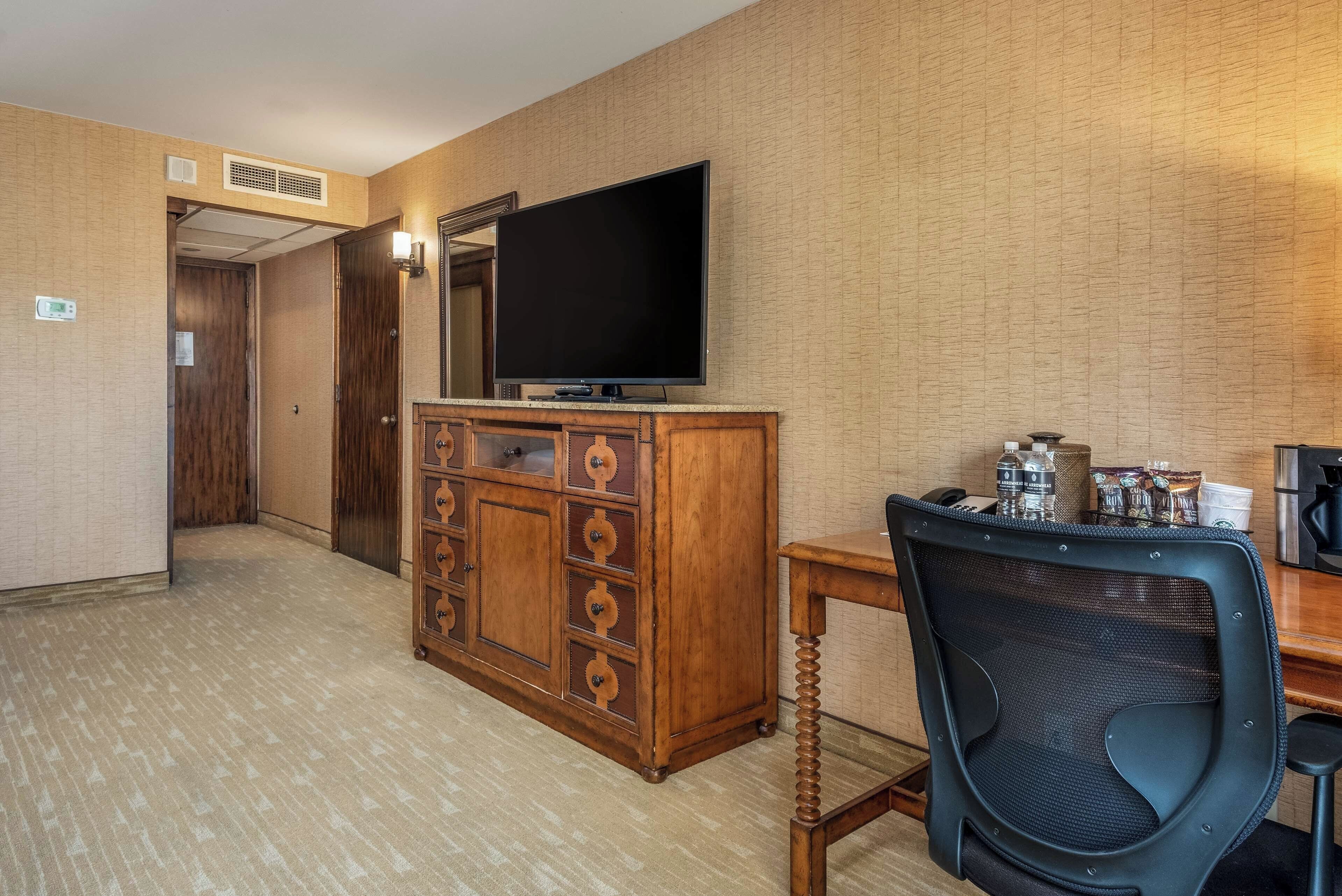 A hotel room with a wooden cabinet, a television, a desk with a chair, and a coffee maker.